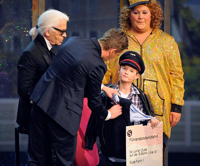 Im Schaffner-Kostüm und begleitet von seinen Wettpaten, Karl Lagerfeld und Cindy aus Marzahn, geht es neben Markus Lanz auf die Bühne.