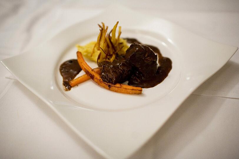 4. GANG: Daube de boef a la provencale &ndash; Polenta &ndash; glasierte Möhrchen. Die Rinderschulter ist so zart geschmort, dass das Fleisch beinah von selbst auf die Gabel fällt. Wie Pommes, nur eleganter und raffinierter im Geschmack, sind die kunstvoll drapierten Möhrchen zurechtgemacht. Brombeere und Pfeffer bringt die Weinbegleitung am Gaumen zusammen: Ein 2010er-Jahrgang aus dem Minervois vom Weingut &bdquo;Domaine La Prade Mari&ldquo; mit dem klangvollen Namen &bdquo;Chant de l&rsquo;Olivier&ldquo;, der so heißt, weil in der Umgebung des Weinbergs das Flirren und Sirren der Olivenbaumblätter besonders schön zu hören sein soll.