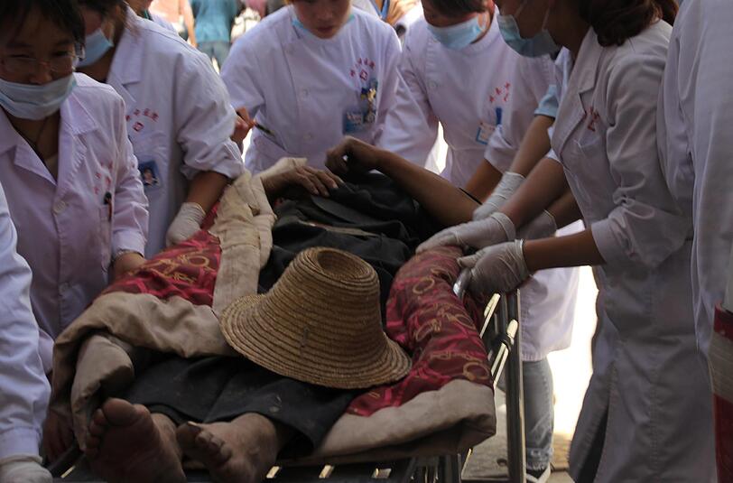 Rettungskräfte versuchen einer verletzten Frau außerhalb eines Krankenhauses in Minxian zu helfen.