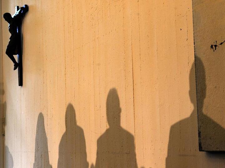 Schatten sind neben einem Holzkreuz mit gekreuzigtem Jesu an einer Wand abgebildet. Foto: Harald Tittel/Archiv
