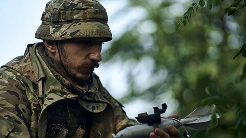 Ein ukrainischer Soldat lädt eine Bombe auf eine Drohne.