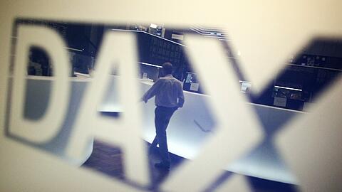 Ein Händler geht über das Parkett in der Börse in Frankfurt am Main und spiegelt sich dabei in einem Logo des Deutschen Aktienindexes (Dax). Foto: Fredrik von Erichsen