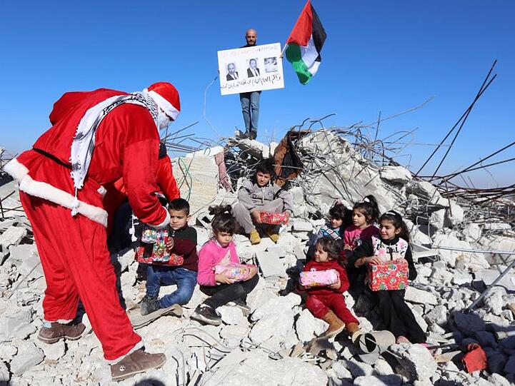 Ein Palästinenser im Weihnachtsmannkostüm verteilt Geschenke und Süßigkeiten an Kinder, die auf den Überresten zerstörter Häuser sitzen.