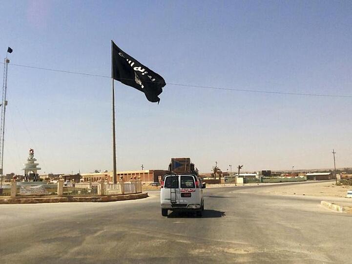 Ein Kleintransporter fährt an einer IS-Flagge vorbei. Foto: Uncredited/AP/dpa/Archivbild