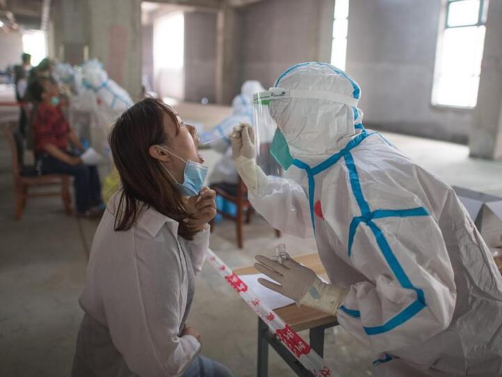 Eine Frau wird in Wuhan von einer Person in Schutzanzug auf das Coronavirus getestet. Wissenschaftler haben in der chinesischen Metropole Freiwilligen den Wirkstoff Ad5-nCoV verabreicht und berichten von ersten Erfolgen.
