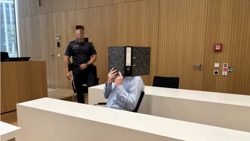 Der Angeklagte versteckt sich hinter einem Aktenordner. Der Angeklagte versteckt sich hinter einem Aktenordner.