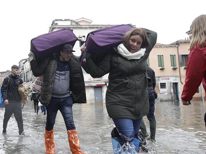 Touristen tragen ihr Gepäck durchs Hochwasser.