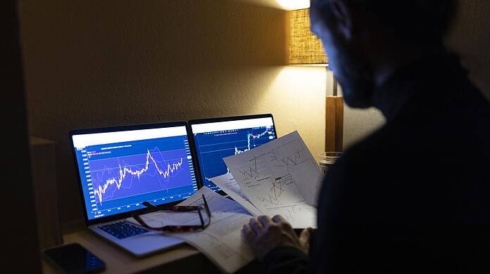 Ein Mann sitzt vor zwei Bildschirmen mit Aktienkursen. Wer investieren will, kann das mit Aktien-ETF-Indexfonds ganz einfach.