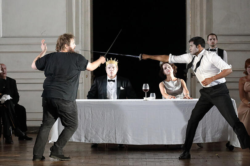 Hamlet (Allan Clayton, li.) im finalen Duell mit Laertes (Sean Panikkar) - einer Intrige seines Onkels, des Königs Claudius (Rod Gilfrey, mit Sophie Koch als Gertrude).