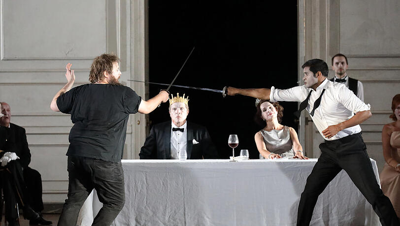 Hamlet (Allan Clayton, li.) im finalen Duell mit Laertes (Sean Panikkar) - einer Intrige seines Onkels, des Königs Claudius (Rod Gilfrey, mit Sophie Koch als Gertrude). Hamlet (Allan Clayton, li.) im finalen Duell mit Laertes (Sean Panikkar) - einer Intrige seines Onkels, des Königs Claudius (Rod Gilfrey, mit Sophie Koch als Gertrude).
