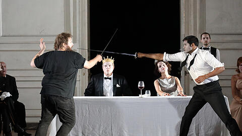 Hamlet (Allan Clayton, li.) im finalen Duell mit Laertes (Sean Panikkar) - einer Intrige seines Onkels, des Königs Claudius (Rod Gilfrey, mit Sophie Koch als Gertrude).