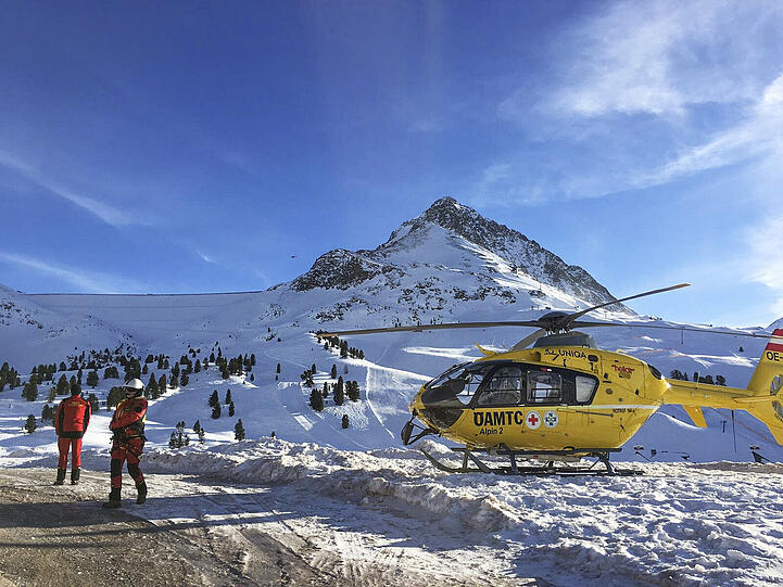 Zwei Rettungshelfer stehen neben einem Helikopter. Bei einem Lawinenabgang unweit der deutsch-österreichischen Grenze konnten nach Polizeiangaben mindestens vier Menschen gerettet werden, eine Person ist gestorben.