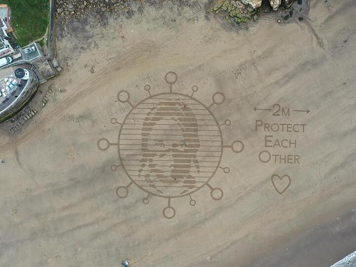 Am Strand in der Stadt Whitby wurde in den Sand ein riesiges Kunstwerk gemalt, das auf den Mindestabstand von zwei Metern während der Corona-Pandemie hinweist.