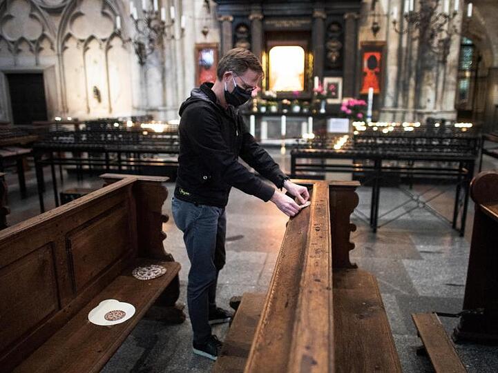 Ein Mitarbeiter der Dombauhütte klebt Aufkleber auf Kirchenbänke im Kölner Dom. Die runden Sticker sollen den Platz markieren, auf den Gottesdienstbesucher sich setzen dürfen.