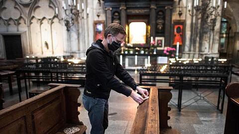 Ein Mitarbeiter der Dombauhütte klebt Aufkleber auf Kirchenbänke im Kölner Dom. Die runden Sticker sollen den Platz markieren, auf den Gottesdienstbesucher sich setzen dürfen.