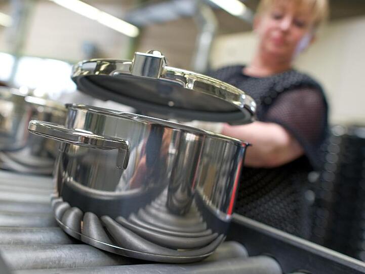 Eine Mitarbeiterin setzt im Stammwerk des Küchengeräteherstellers Württembergische Metallwarenfabrik AG (WMF) in Geislingen einen Deckel auf einen fertiggestellten Topf.