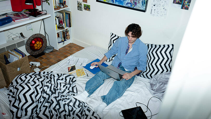 Ein Student sitzt in seinem Bett am Laptop (Symbolbild).