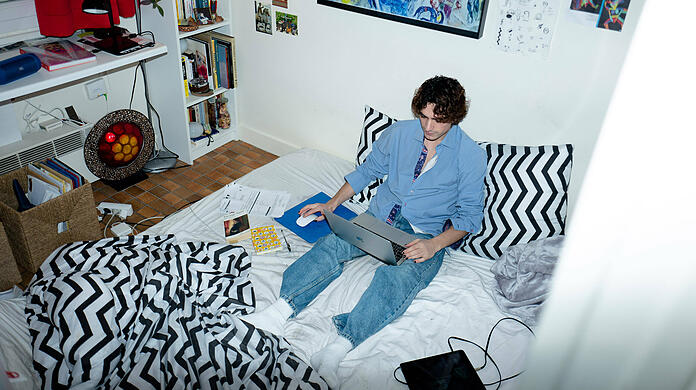 Ein Student sitzt in seinem Bett am Laptop (Symbolbild).