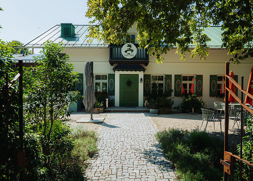 Das Wirtshaus Hans Xaver in Oberhaching. Hinten erstreckt sich der Biergarten, die Kugler Alm. Der Radlweg führt direkt zwischen Parkplatz und dem Eingang vorbei.