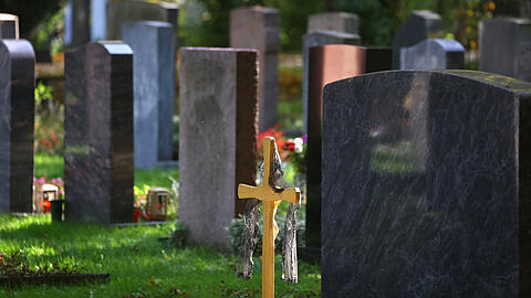 Der Friedhof als (bisheriger) Standard der Trauer: Ein Kreuz steht vor Grabsteinen in Augsburg.