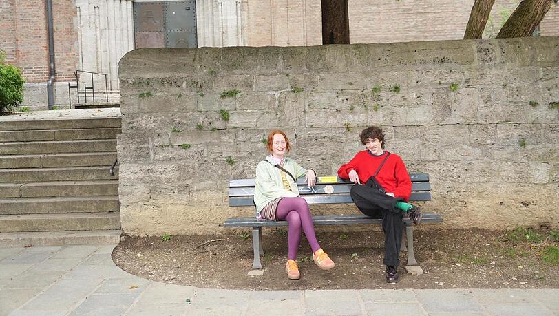 Designerin Ruth (23) und Model Liam (23) probieren das neue Ratschbankerl am St.-Anna-Platz im Lehel schon einmal aus. Von den speziell markierten Parkbänken gibt es jetzt in jedem Stadtbezirk eine.