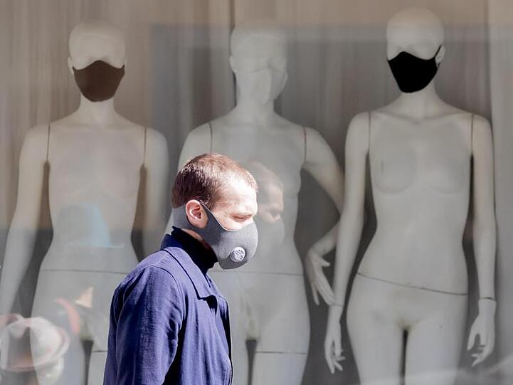 Ein Mann mit Schutzmaske läuft an einem Schaufenster mit Schaufensterpuppen, die Stoffmasken tragen, vorbei. Foto: Christoph Soeder/dpa/Archivbild