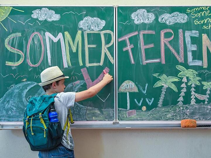 Der Schüler Ben aus der Klasse 2A malt in seinem Klassenraum an einer Tafel mit der Aufschrift "Sommerferien". Foto: Patrick Pleul/Archivbild