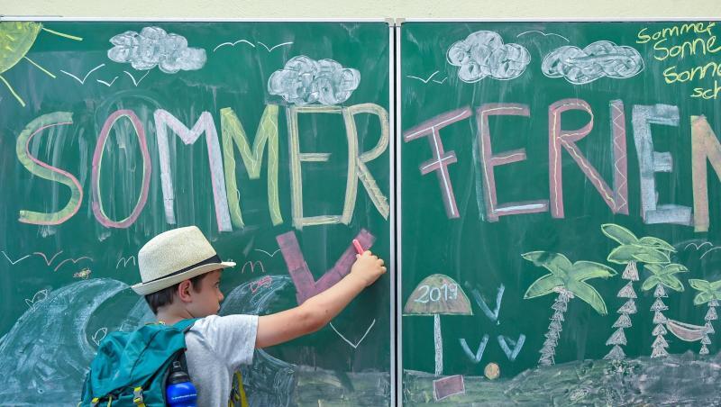 Der Schüler Ben aus der Klasse 2A malt in seinem Klassenraum an einer Tafel mit der Aufschrift "Sommerferien". Foto: Patrick Pleul/Archivbild Der Schüler Ben aus der Klasse 2A malt in seinem Klassenraum an einer Tafel mit der Aufschrift "Sommerferien". Foto: Patrick Pleul/Archivbild