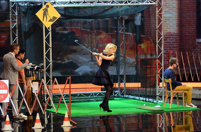 Schauspielerin Maria Furtwaengler schlägt mit einem Golfschlaeger, während Wettkandidat Jonas Greiner (r.) versucht, den Balltyp am Geraeusch zu erkennen.