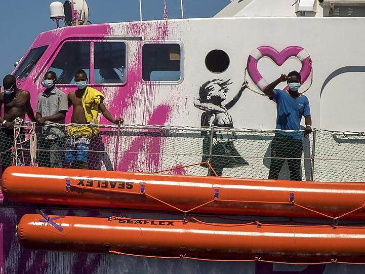 Ein Junge an Bord der "Louise Michel" winkt der Besatzung des Rettungsschiffes "Astral" zu. Das Rettungsschiff "Louise Michel" kann sich nach Angaben der Besatzung mit mehr als 200 Migranten an Bord nicht länger sicher fortbewegen.