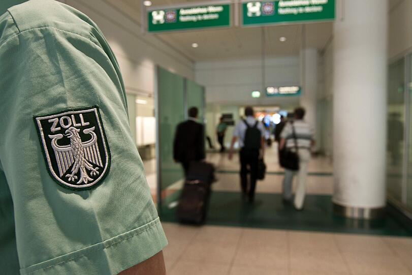 Ein Zollbeamter steht im Flughafen München vor dem Durchgang zum Zoll.
