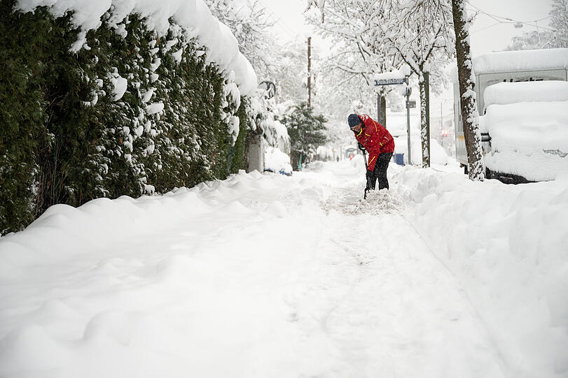 Ein Mann räumt Schnee von einem Gehweg vor seinem Haus.