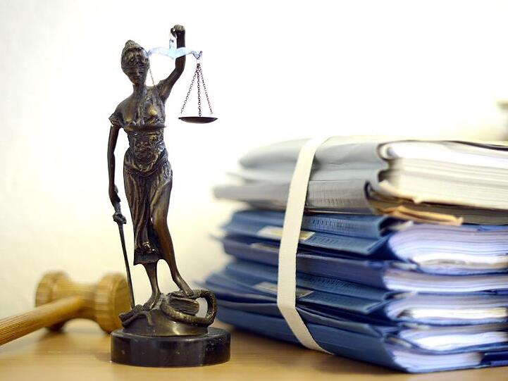 Die Nachbildung der Justitia steht neben einem Holzhammer und Akten.