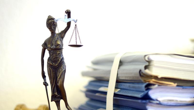 Die Nachbildung der Justitia steht neben einem Holzhammer und Akten. Die Nachbildung der Justitia steht neben einem Holzhammer und Akten.