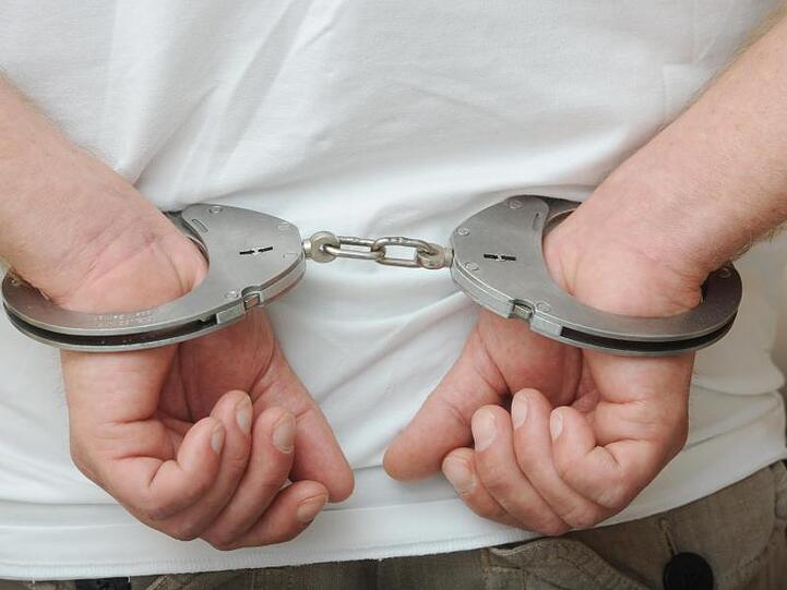 Zwei männliche Hände sind in Polizeihandschellen gefesselt. Foto: Uli Deck/dpa/Archivbild