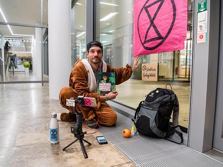 Extinction-Rebellion-Aktivist Thomas Nier klebt mit der Hand an einer Scheibe der Siemens Zentrale. Foto: Matthias Balk/dpa