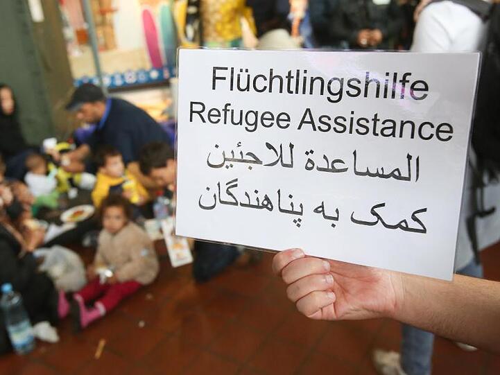 Ein freiwilliger Helfer hält 2015 im Hauptbahnhof in Hamburg ein Schild auf deutsch, englisch und arabisch, auf der Hilfe für Flüchtlinge angeboten wird.