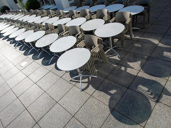 Tische und Stühle eines Straßencafes sind in der Sonne aufgereiht. Foto: Stefan Puchner/dpa/Symbolbild