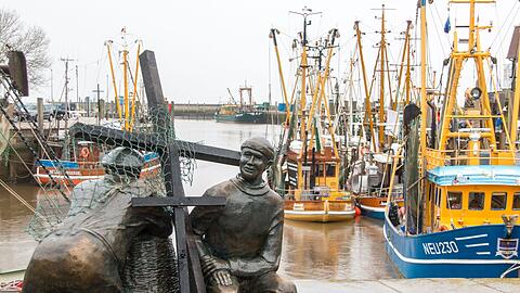 Schwarze Holzkreuze lehnen an der Bronezeskulptur "Alt- und Jungfischer" im Hafen in Neuharlingersiel. Das Fischen mit Grundschleppnetzen steht in der Kritik.