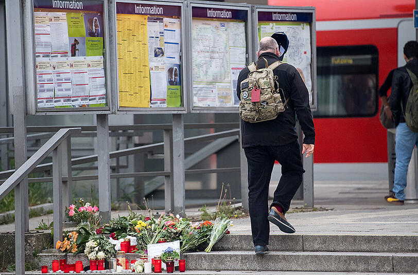 Blumen und Kerzen liegen am Bahnhof in Grafing um ein handgemaltes Schild. Bei einer Messerattacke waren am Dienstag drei Personen verletzt und ein Mann getötet worden.