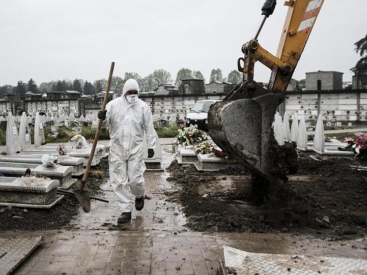 Ein Mitarbeiter im Schutzanzug geht in der Industriestadt Turin über einen Friedhof, auf dem frische Gräber ausgehoben werden.