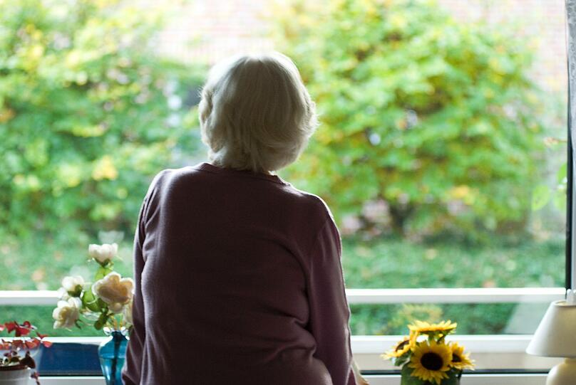 Sie ist auf die Ehrlichkeit ihres Pflegers angewiesen: Eine ältere Frau sitzt am Fenster ihrer Wohnung.