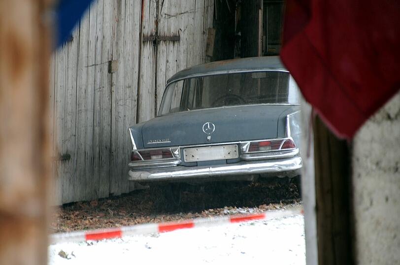 Halb in der Garage steht ein uralter Mercedes.