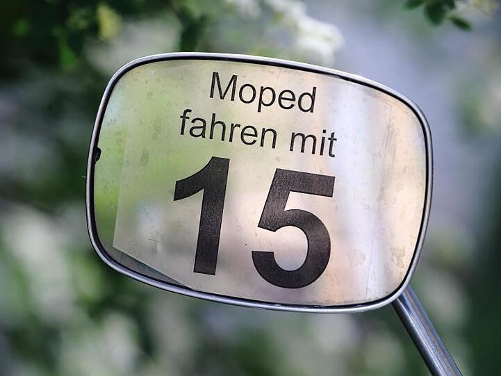 Der Schriftzug "Moped fahren mit 15" ist an dem Spiegel eines Mopeds angebracht. Foto: Jens Wolf/dpa/Illustration