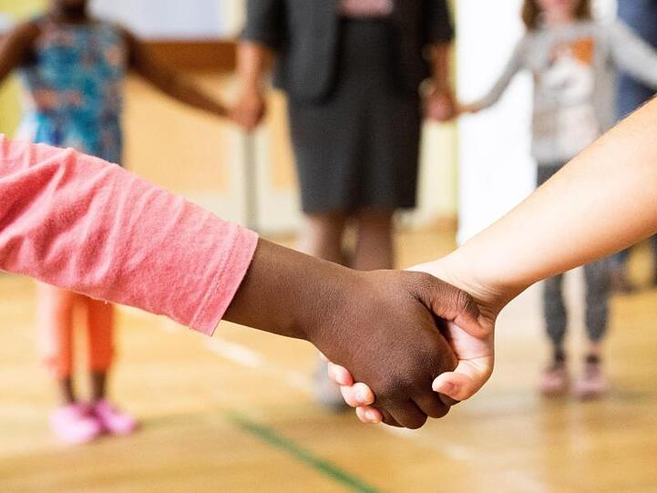 Hand in Hand tanzen Kinder und Erzieherinnen bei einem Bewegungsspiel in einer Turnhalle.