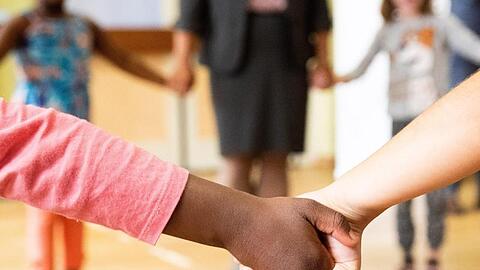 Hand in Hand tanzen Kinder und Erzieherinnen bei einem Bewegungsspiel in einer Turnhalle.