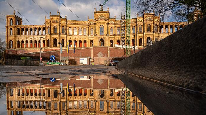 Der Bayerische Landtag spiegelt sich nach einem Regenschauer in einer Pfütze auf der Maximiliansbrücke.