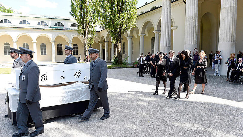 Vier Sargträger bringen den weißen Sarg (mit schwarzen Käfern), wie es sich der Feinkost-König gewünscht hat, zum Friedhof. Vier Sargträger bringen den weißen Sarg (mit schwarzen Käfern), wie es sich der Feinkost-König gewünscht hat, zum Friedhof.