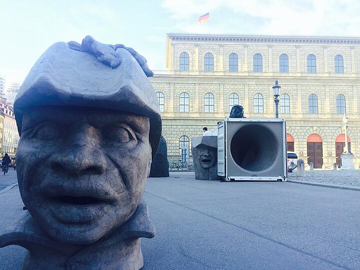 Riesenköpfe aus Pappe überraschen derzeit Passanten am Max-Joseph-Platz.
