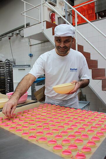Die rosafarbenen Herzen werden von einem Mitarbeiter liebevoll mit goldenen Zuckerperlen verziert.